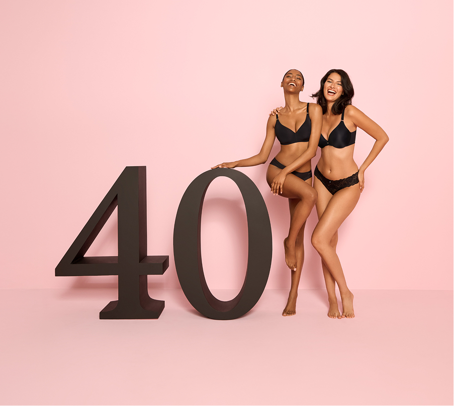 Two models dressed in black bras and panties standing beside a “40” sign to celebrate la Vie en Rose’s 40th anniversary