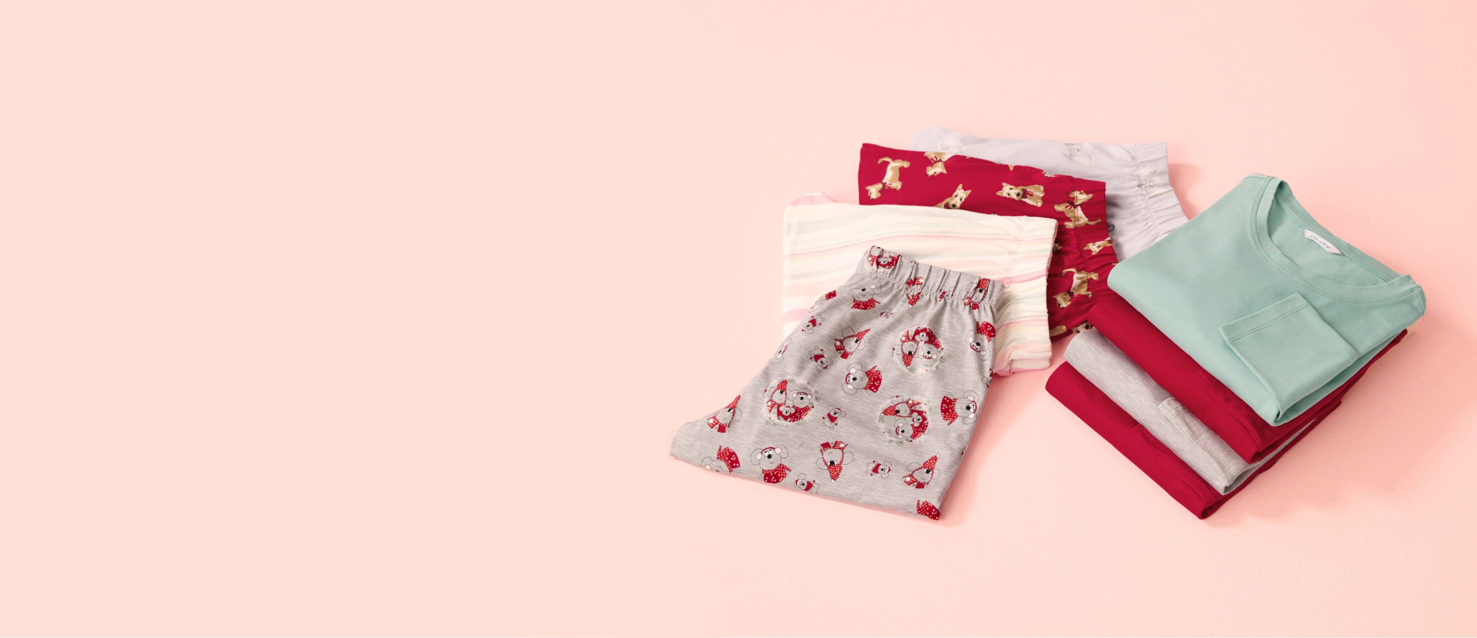 Several pajamas in various colors, folded on a pink background