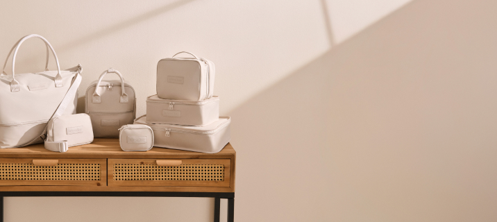 Seven beige travel accessories, including bags, pouches, and cases, placed on a table