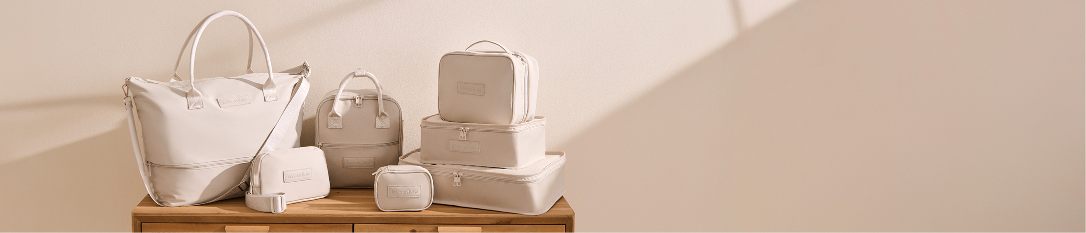 Seven beige travel accessories, including bags, pouches, and cases, placed on a table